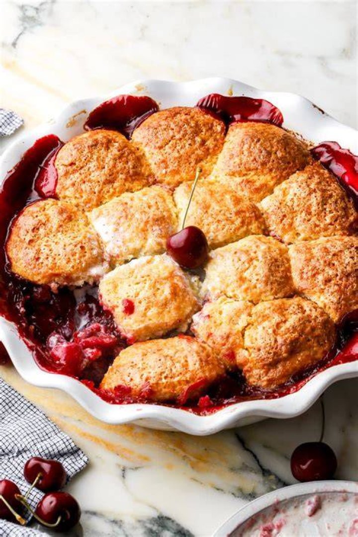 Cherry cobbler in a white bowl topped with vanilla ice cream.