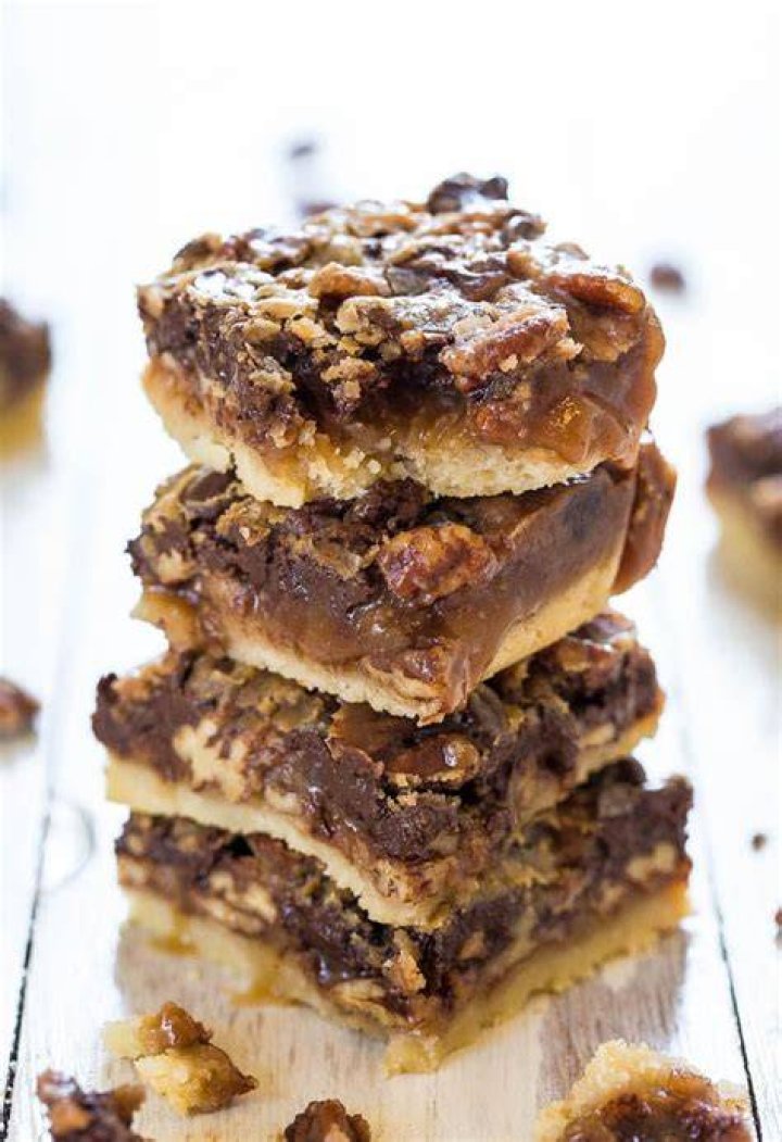 Stack of chocolate pecan bars on white parchment paper.